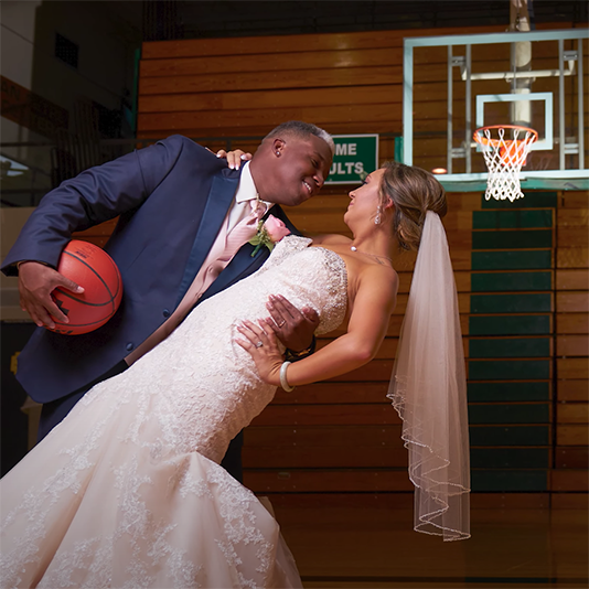 A groom hold his bride and a basketball on the Bryan High court